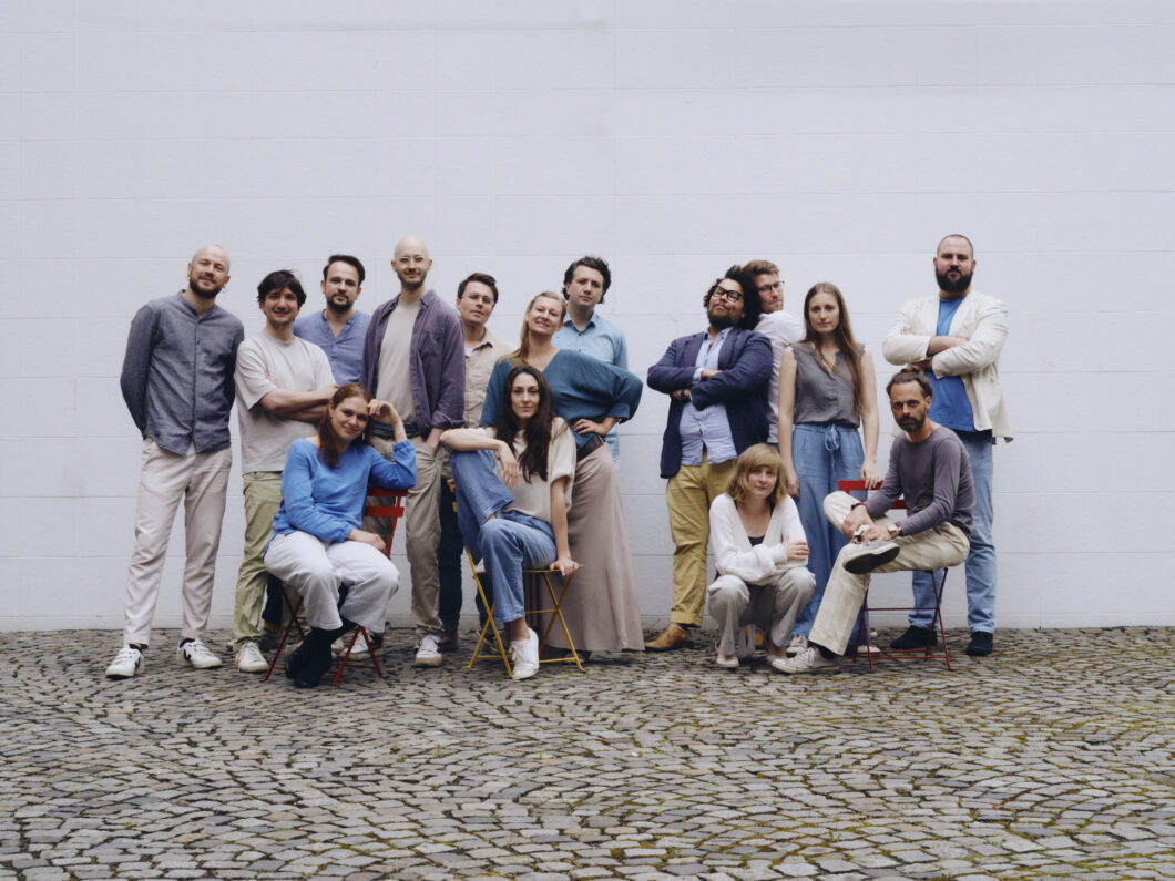 Eine Gruppe Menschen posiert vor einer weißen Wand, es ist das hannoversche Orchester im Treppenhaus.