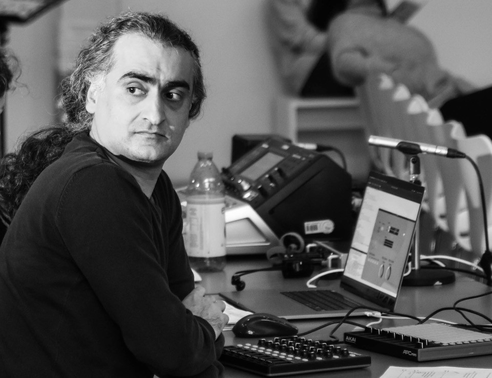 Schwarz-weiß-Foto eines Mannes, der an einem Schreibtisch sitzt und über die rechte Schulter an der Kamera vorbeischaut. Es ist Ehsan Khatibi.