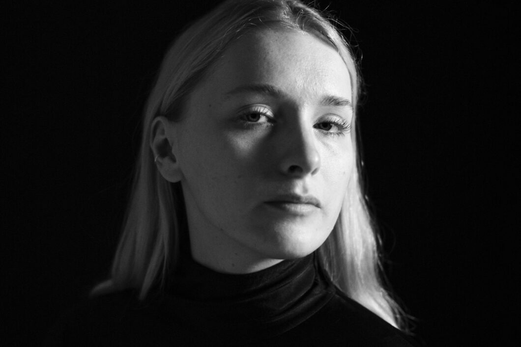 Schwarz-weiß-Portrait einer jungen Frau mit hellen, schulterlangen Haaren im schwarzen Rollkragenpullover, es ist Komponistin Kate Milligan.