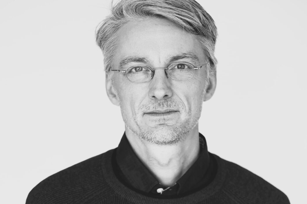 Schwarz-weiß-Porträtfoto eines Mannes mit hellen Haaren und randloser Brille in dunklem Hemd. Es ist Komponist Einar Torfi Einarsson.
