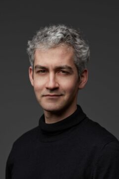 Ein Mann mit grauen, kurzen Haaren und im schwarzen Rollkragen-Pullover lächelt in die Kamera; es ist Manuel Durão.