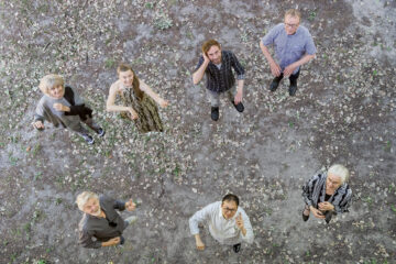 Sieben Menschen, von oben fotografiert, halten imaginäre Instrumente, es ist das Ensemble L'ART POUR L'ART.