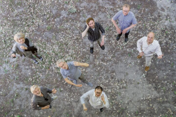 Sieben Menschen, von oben fotografiert, halten imaginäre Instrumente, es ist das Ensemble L'art pour l'art.