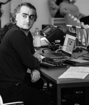 Schwarz-weiß-Foto eines Mannes, der an einem Schreibtisch sitzt und über die rechte Schulter an der Kamera vorbeischaut. Es ist Ehsan Khatibi.