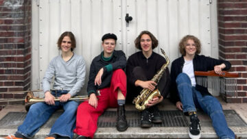 Vier junge Menschen sitzen mit Instrumenten in den Händen vor einem weißen Garagentor