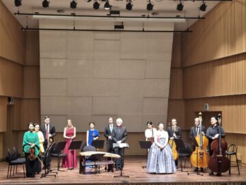 Musiker*innen in bunten Kleidern und mit Instrumenten stehen in einem Konzertraum; es ist das Daegu Concert House Ensemble.