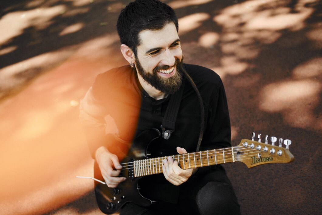 Ein junger Mann mit schwarzen Haaren und Vollbart spielt lächelnd eine E-Gitarre. Es ist der Musiker Francesco Palmieri.