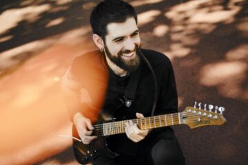 Ein junger Mann mit schwarzen Haaren und Vollbart spielt lächelnd eine E-Gitarre. Es ist der Musiker Francesco Palmieri.