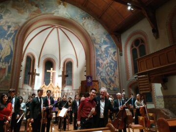 Ein Orchester in einer Kirche, zwei Musiker umarmen sich.