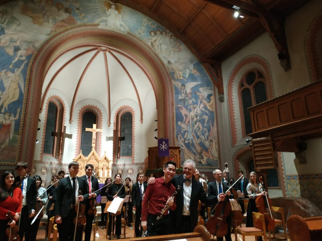 Ein Orchester in einer Kirche, zwei Musiker umarmen sich.