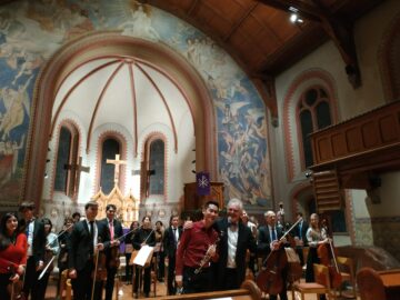 Ein Orchester in einer Kirche, zwei Musiker umarmen sich.