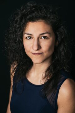 Portrait einer jungen Frau mit dunklen Locken vor schwarzem Hintergrund. Es ist Marijana Janevska