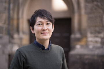 Ein Mann mit schwarzen kurzen Haaren lächelt in die Kamera. Es ist Komponist Tomoya Yokokawa.
