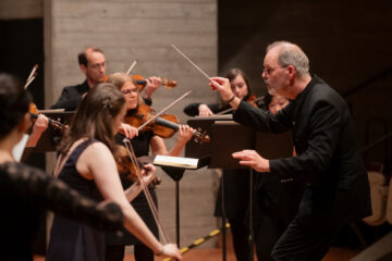 Ein Mann mit kurzen grauen Haaren dirigiert ein Orchester; es ist Thorsten Encke.