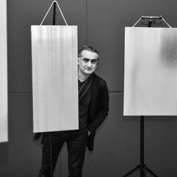 Schwarz-weiß-Foto eines Mannes, der hinter einer grauen Leinwand hervorlugt. Es ist Komponist Ehsan Khatibi.