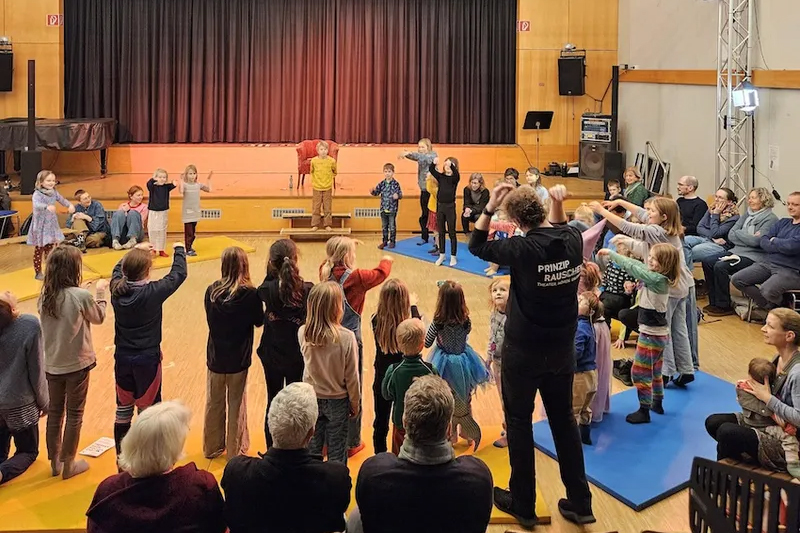 Kinder tanzen in einem Saal, im Hintergrund eine Bühne